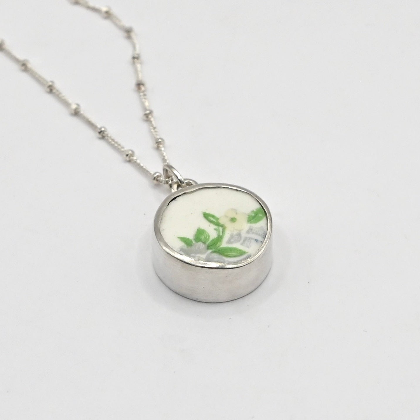 Silver necklace with a round pendant featuring floral design on a light gray background