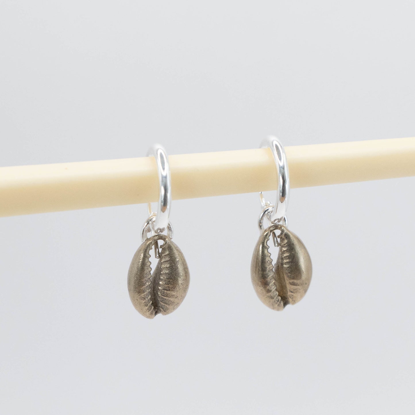 Cowry Shell Hoop Earrings - brass cowry pair hanging on display rod showing drop length