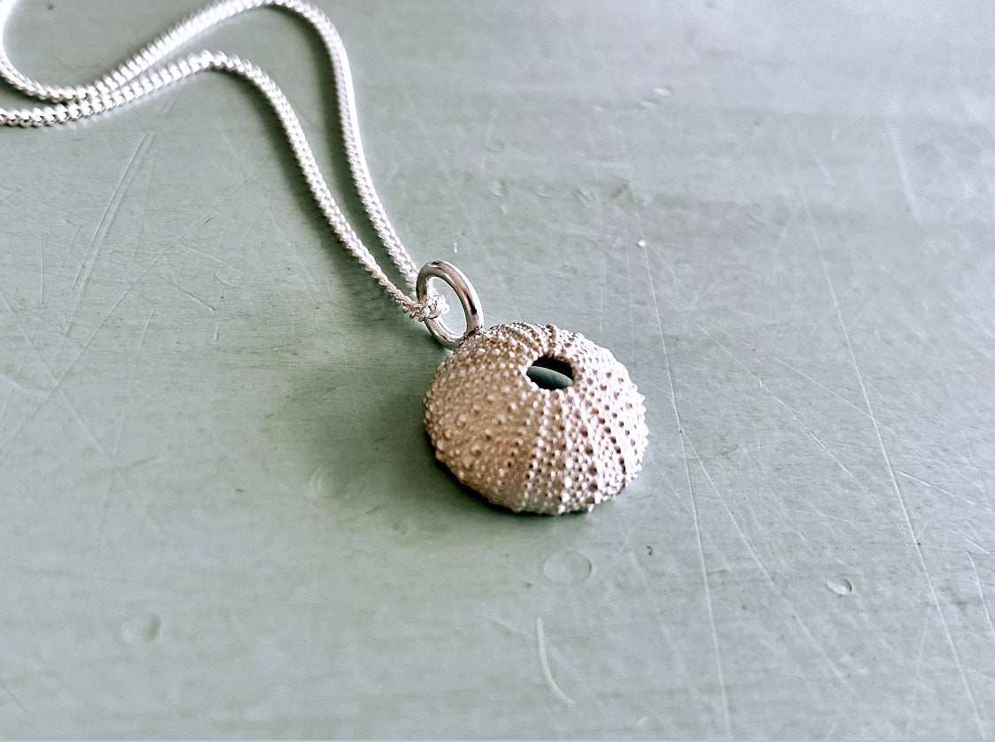 Sterling silver sea urchin pendant hanging on a silver chain, showcased on a grey surface.