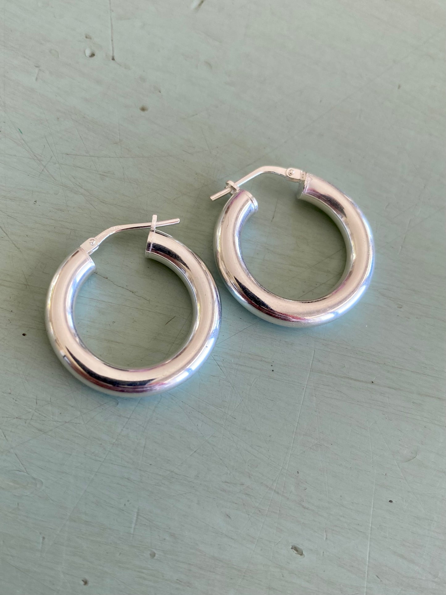 Close-up of polished sterling silver hoop earrings showcasing their simple clasp and elegant thickness.