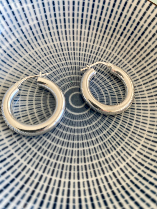 Sterling silver hoop earrings resting on a blue and white patterned surface, highlighting their circular design