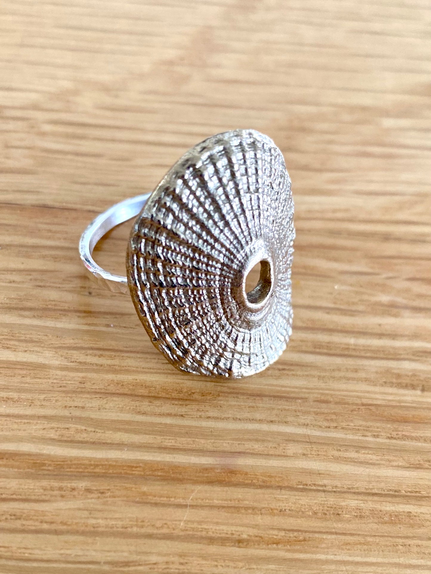 Silver textured shell ring placed on a wooden surface, showcasing detailed craftsmanship