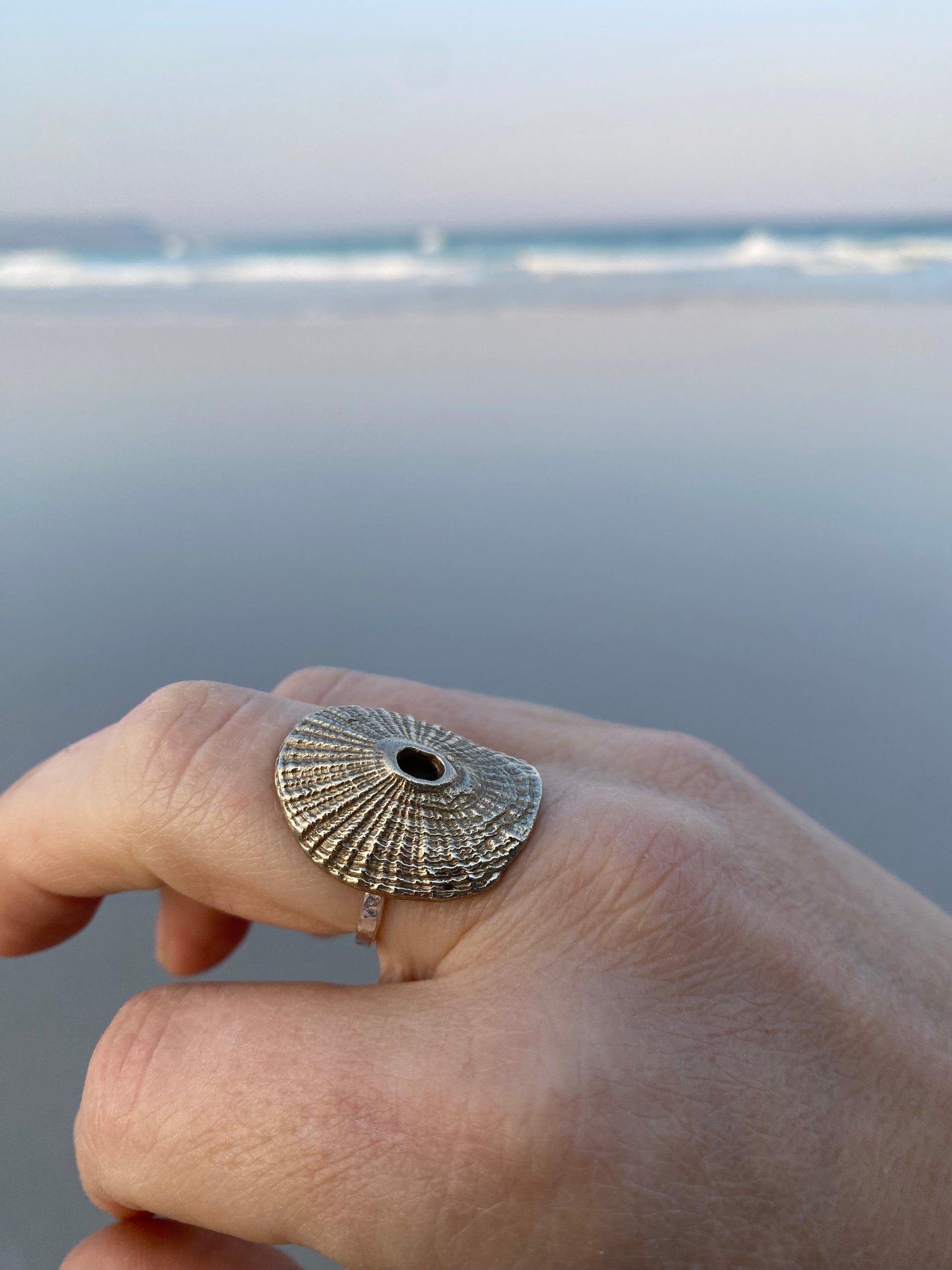Hand modeling a textured Santa Maria shell ring with ocean waves in the soft-focus background.