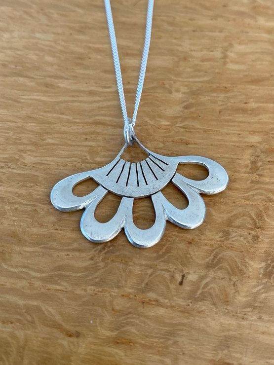 Close-up of a silver Lotus-inspired Flower Pendant on a wooden surface, highlighting the elegant design