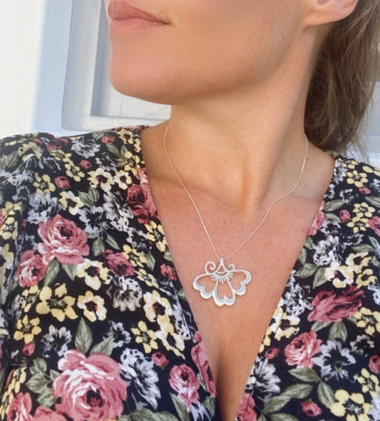 Woman wearing a large lotus-inspired sterling silver pendant, complementing a floral print dress for a harmonious, nature-inspired look.
