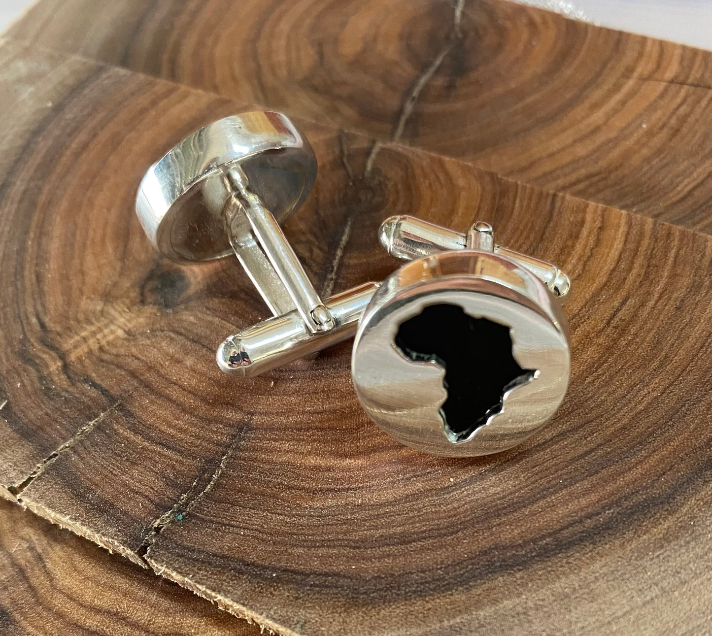 Elegant silver Africa-shaped cufflinks displayed on wooden surface for a rustic look.