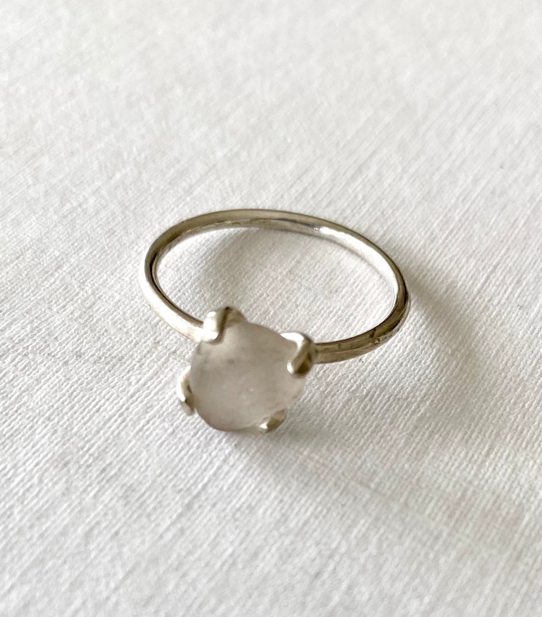 Elegant sterling silver ring featuring a soft white sea glass nugget, highlighted against a textured white backdrop.