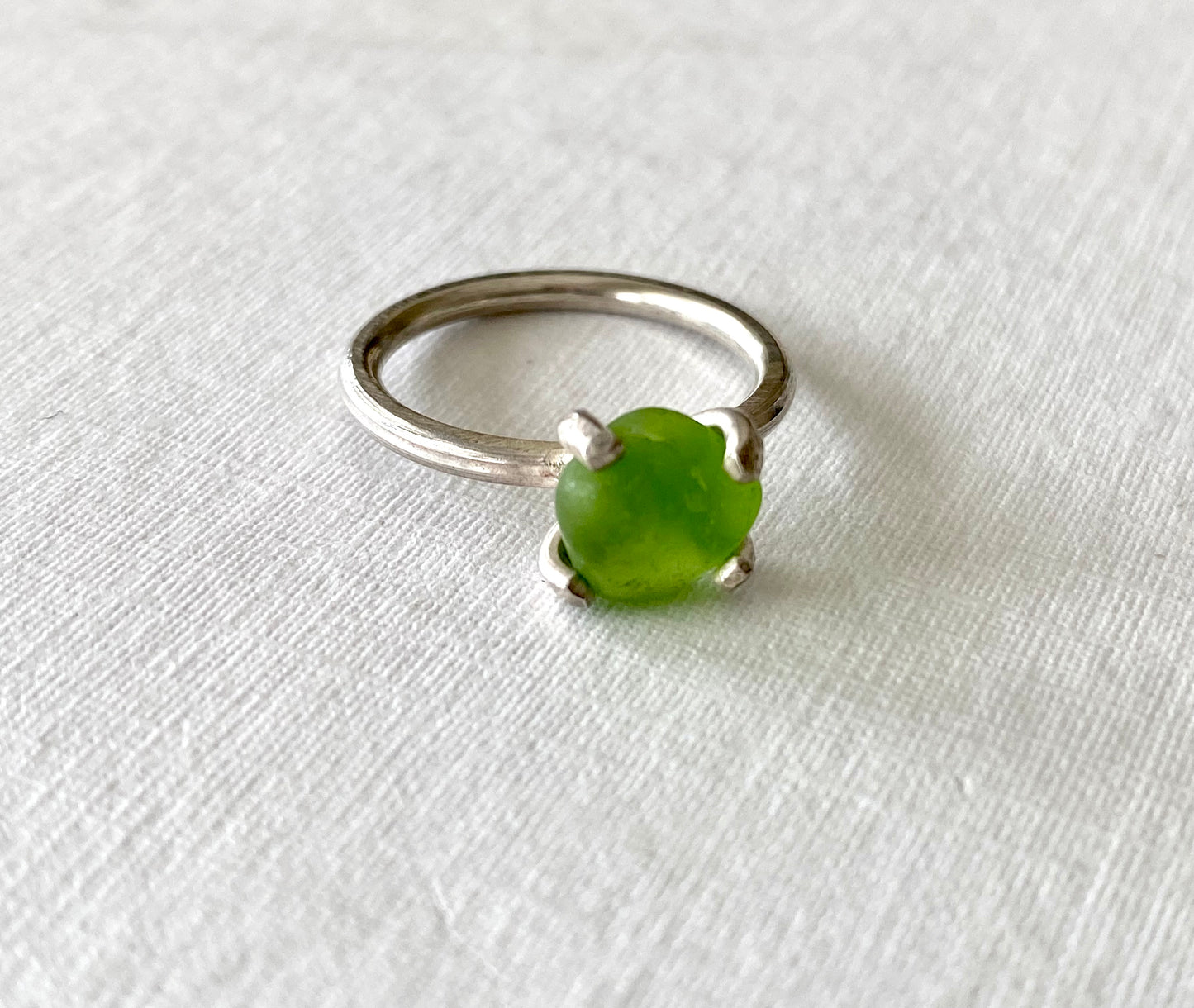 Close-up of a handmade ring with a vibrant green sea glass nugget set in a sterling silver band