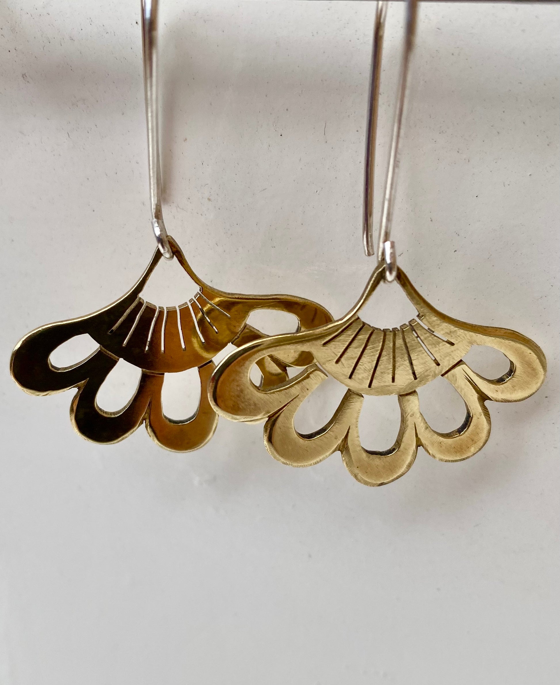 A pair of brass lotus-inspired hook earrings, hanging gracefully with detailed petal design, reflecting a golden hue.