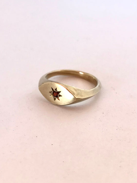 Ladies brass signet ring with a star engraving and a topaz gemstone on a light background.