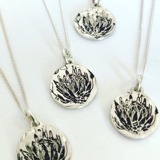 Handcrafted sterling silver pendant featuring an oxidized Protea imprint on a circular disc, displayed on a 45cm chain, representing South African artisan jewelry