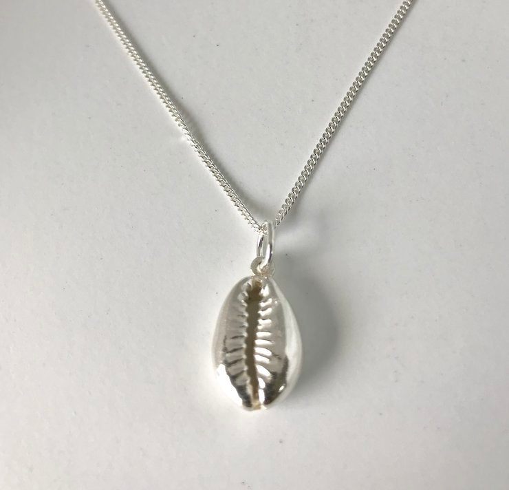 Close-up of a polished sterling silver cowry shell pendant on a fine silver chain against a white background
