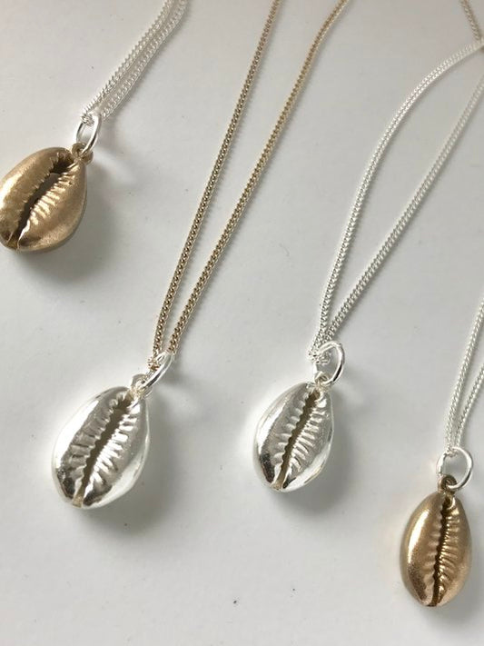Sterling silver and brass cowry shell pendants on matching chains, reflecting a handcrafted finish