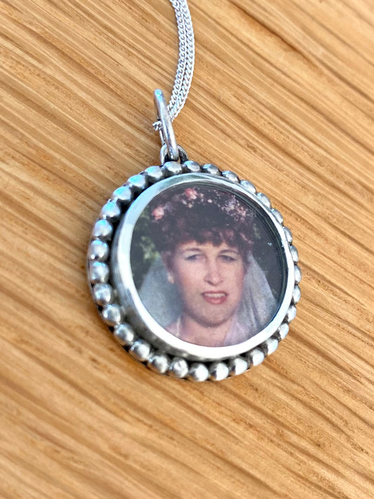 Personalized sterling silver memory necklace with a circular frame featuring a protected photo, displayed on a wooden surface, with a 45cm sterling silver chain.