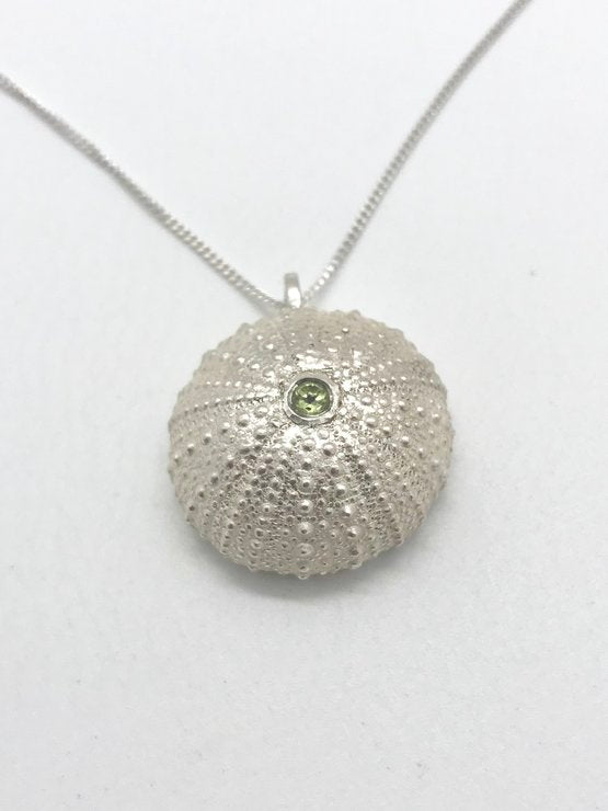Sterling silver sea urchin pendant with a vibrant peridot gemstone on a silver chain, set against a white backdrop