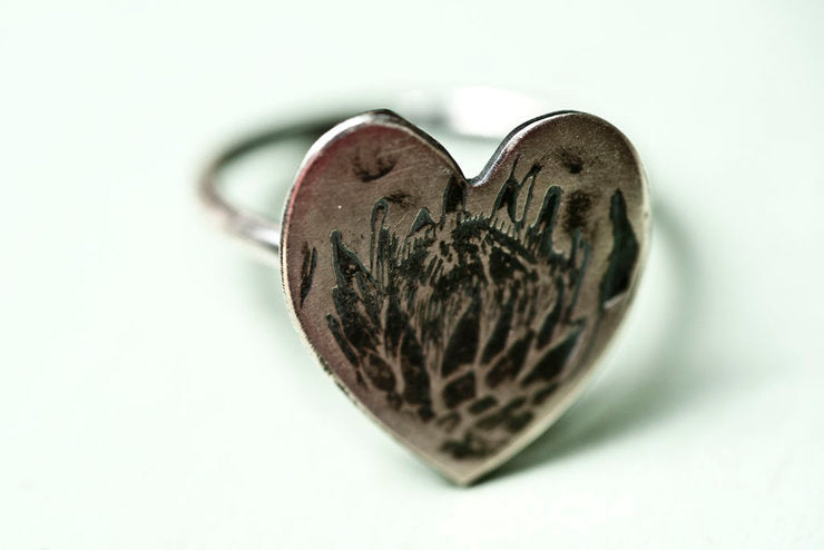 Close-up view of Protea Heart Ring displaying the detailed protea pattern on a darkened silver heart-shaped top.