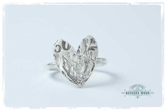 Angled perspective of a sterling silver Protea Heart Ring, highlighting the protea embossment and ring's curvature.