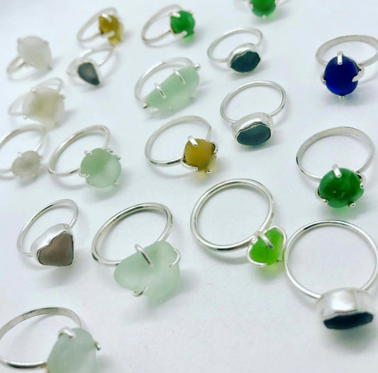 Assortment of sterling silver sea glass rings in various shades, including green, blue, and yellow, displayed on a white background.