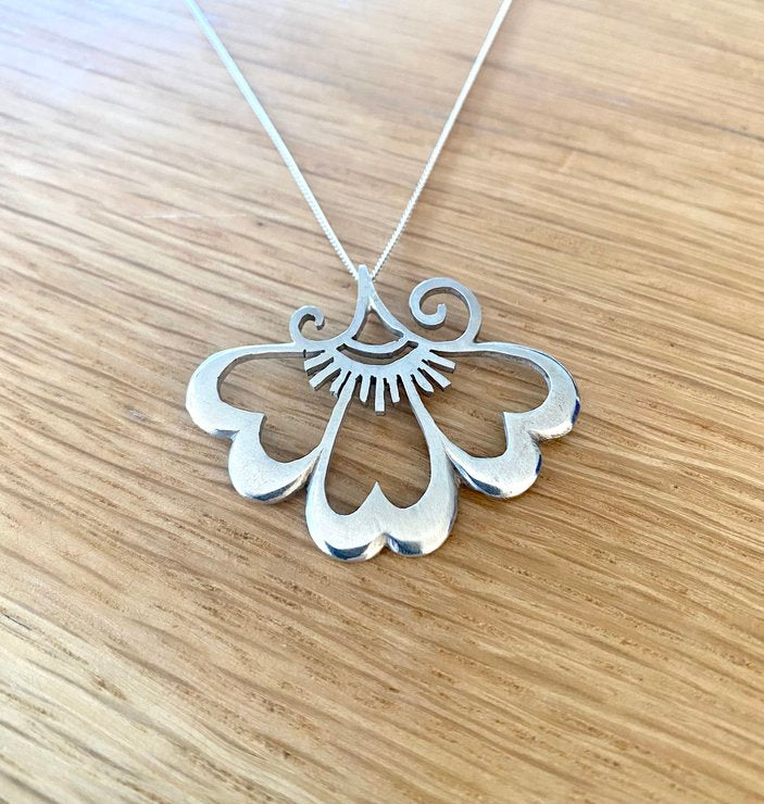 Close-up of a sterling silver lotus flower pendant on a wooden background, showcasing intricate craftsmanship and polished finish.