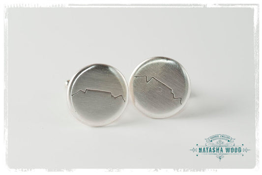 Silver cufflinks with an engraved silhouette of Table Mountain on a white background.