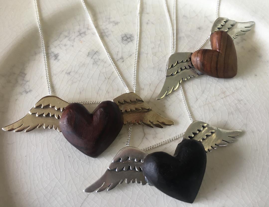 Close-up of the Silver Winged Wooden Heart Pendant against a white fabric background, highlighting the fine details and craftsmanship.