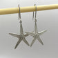 Starfish Earrings - bright sterling silver dangling from display prop, front angle