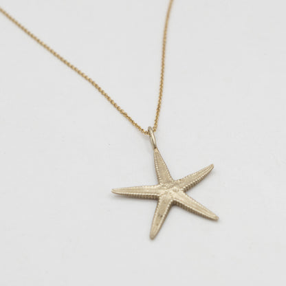 brass Starfish pendant necklace on a light gray background with gold plated chain