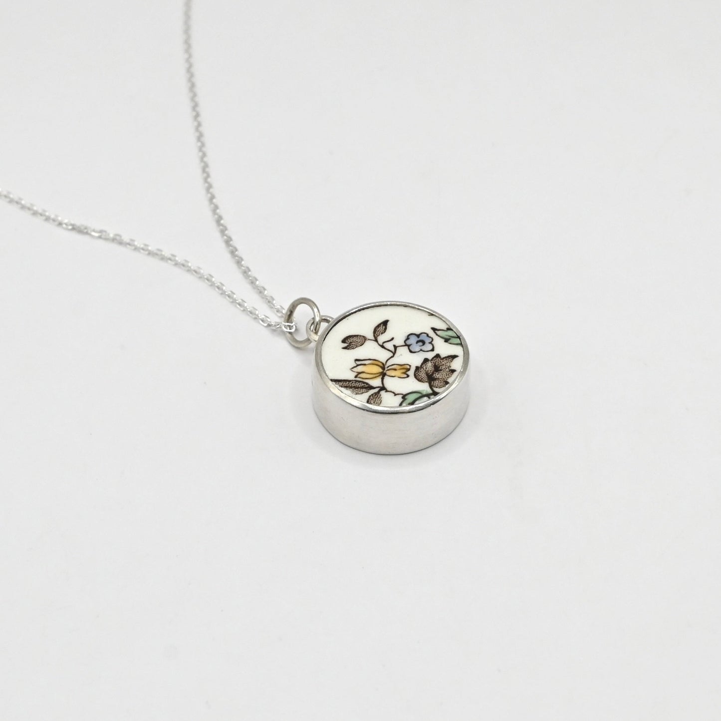 Silver necklace with a round pendant featuring floral design on a white background