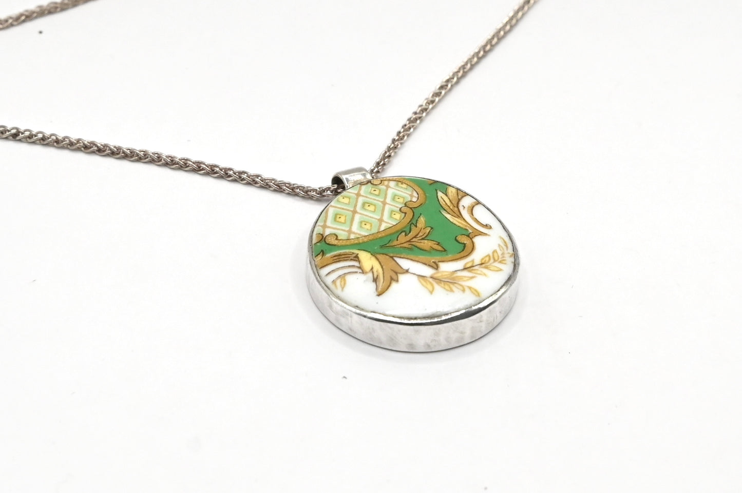 Once Upon a Teacup Pendant - angled front view, green and gold antique bone china pattern in a sterling silver bezel with snake chain