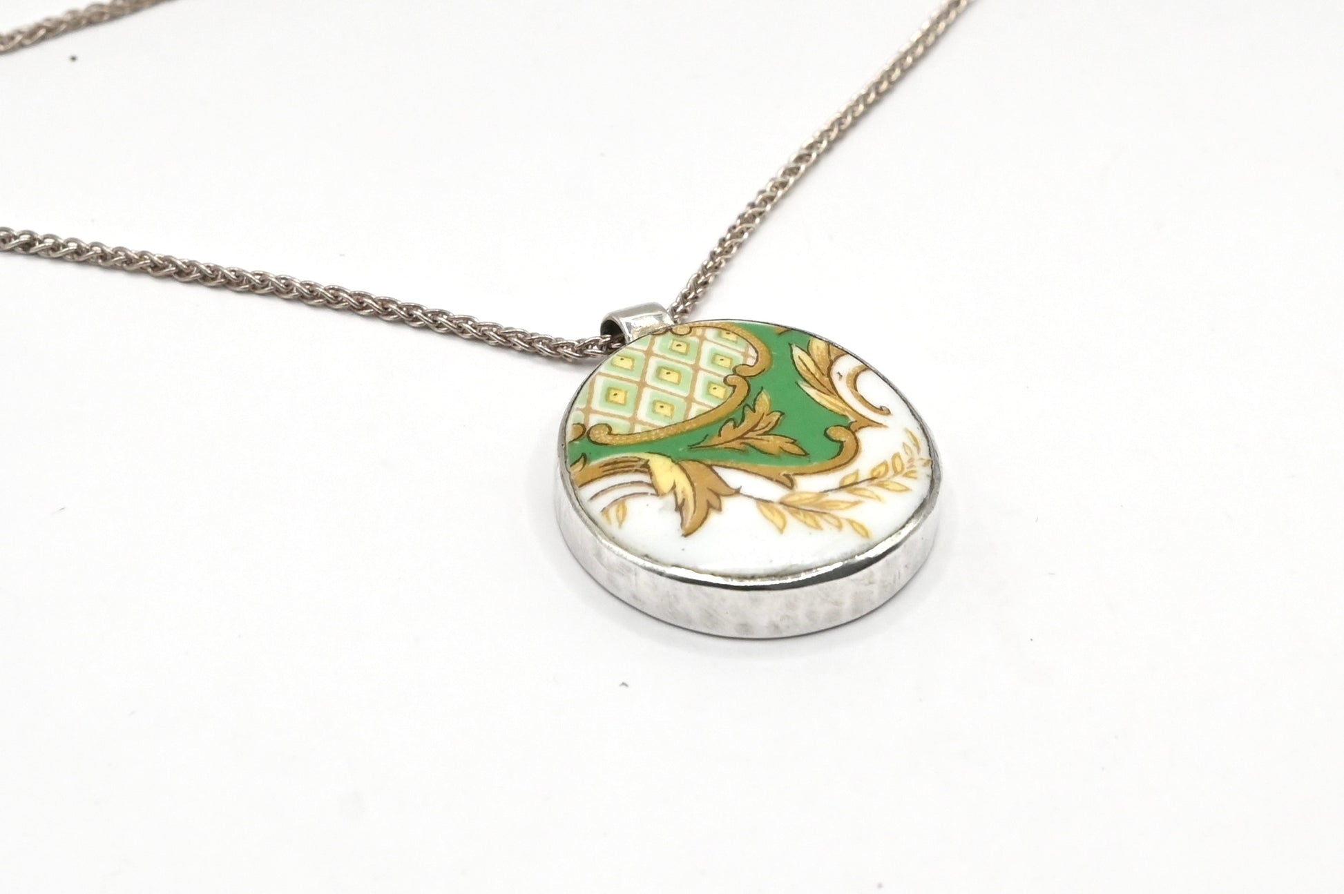 Once Upon a Teacup Pendant - angled front view, green and gold antique bone china pattern in a sterling silver bezel with snake chain