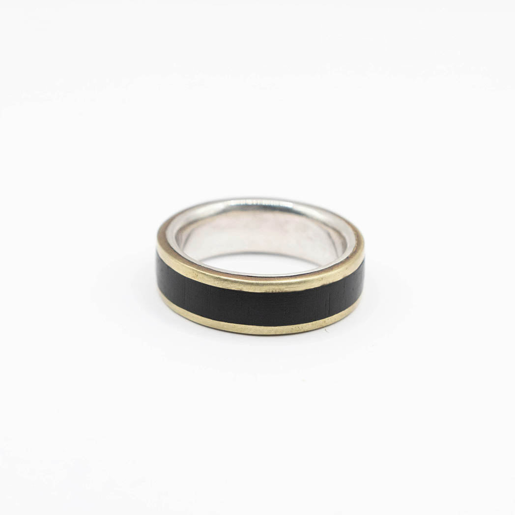 A wide band ring with a silver interior and gold-colored edges. The center of the ring is inlaid with a african black wood, creating a bold and sleek design.