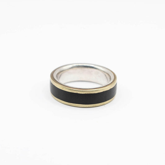 A wide band ring with a silver interior and gold-colored edges. The center of the ring is inlaid with a african black wood, creating a bold and sleek design.