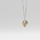 Handmade Brass Cowrie Shell Pendant - front hanging view on grey gradient background, rounded crop