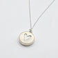 showing the back of the pendant, a heart cut out on silver disc showing the white of the ceramic