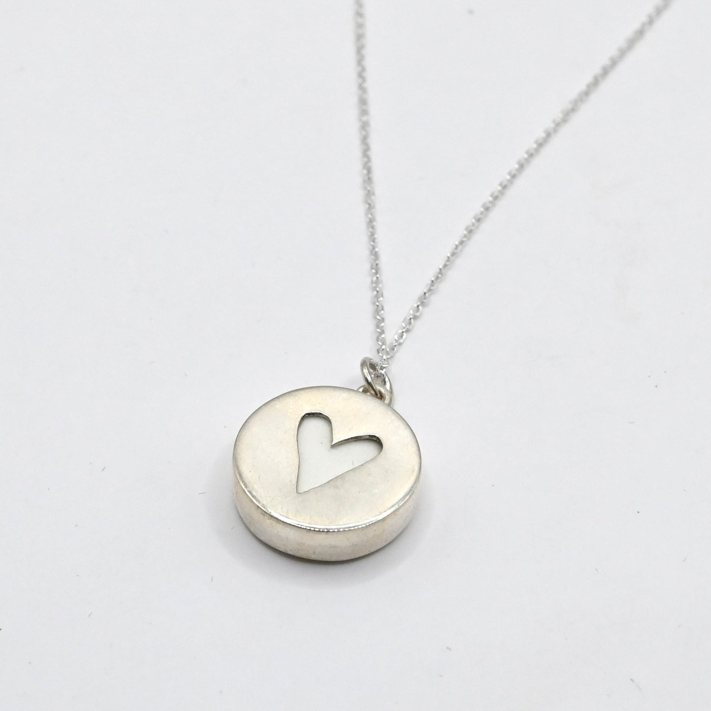 showing the back of the pendant, a heart cut out on silver disc showing the white of the ceramic