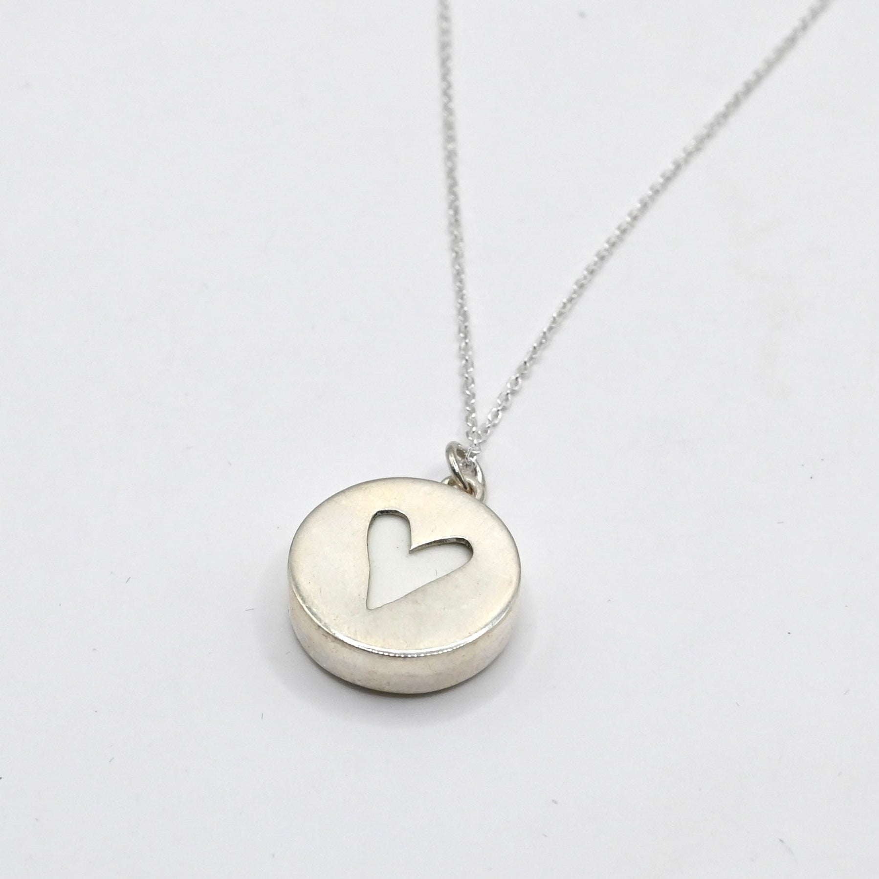 showing the back of the pendant, a heart cut out on silver disc showing the white of the ceramic