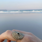 Hand modeling a textured Santa Maria shell ring with ocean waves in the soft-focus background.