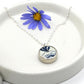 Necklace with a blue and white pendant on a white dish with a purple flower