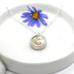 ceramic and silver pendant, presented on a white dish, showing the pink and green floral design on the ceramic and side of the silver bezel setting with a chain.
