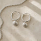 Sterling Silver Scallop Shell Hoop Earrings - pair hanging on display rod, full hoop view by Natasha Wood Jewellery