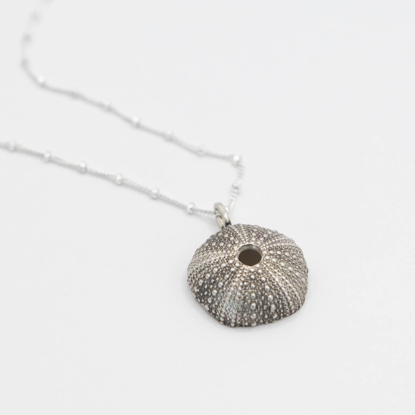 "Intricately crafted oxidized silver sea urchin pendant, hanging from a fine silver chain, showcasing the detailed patterns of the urchin’s textured surface with a subtle antique finish