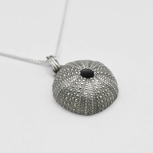 Antique-finish oxidized silver sea urchin pendant with intricate surface detailing, suspended from a delicate silver chain. The darkened silver accentuates the natural texture of the urchin, offering a rustic, elegant charm