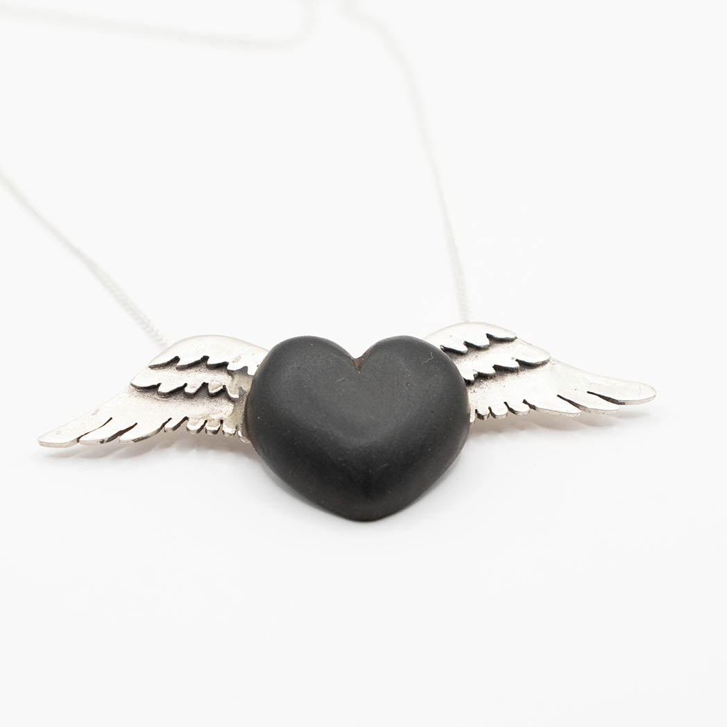 A striking necklace with a heart-shaped pendant carved from rich black wood, adorned with silver wings on either side. The dark wood contrasts sharply with the bright silver, creating a bold and elegant design on a fine silver chain.