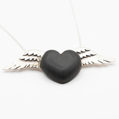 A striking necklace with a heart-shaped pendant carved from rich black wood, adorned with silver wings on either side. The dark wood contrasts sharply with the bright silver, creating a bold and elegant design on a fine silver chain.