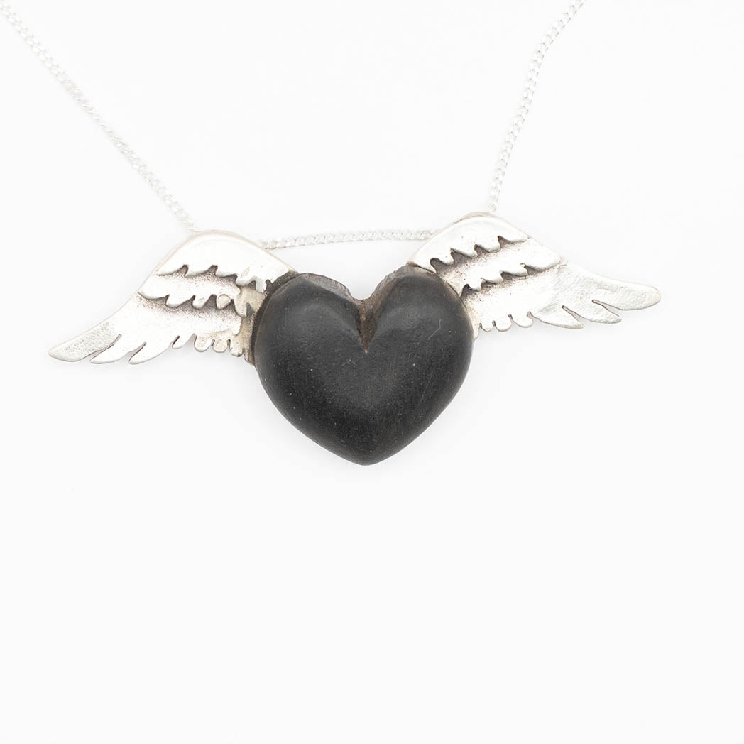 This necklace showcases a black wood heart-shaped pendant, flanked by intricately designed silver wings. The deep, dark tones of the wood provide a striking contrast against the shimmering silver, all suspended on a delicate chain.